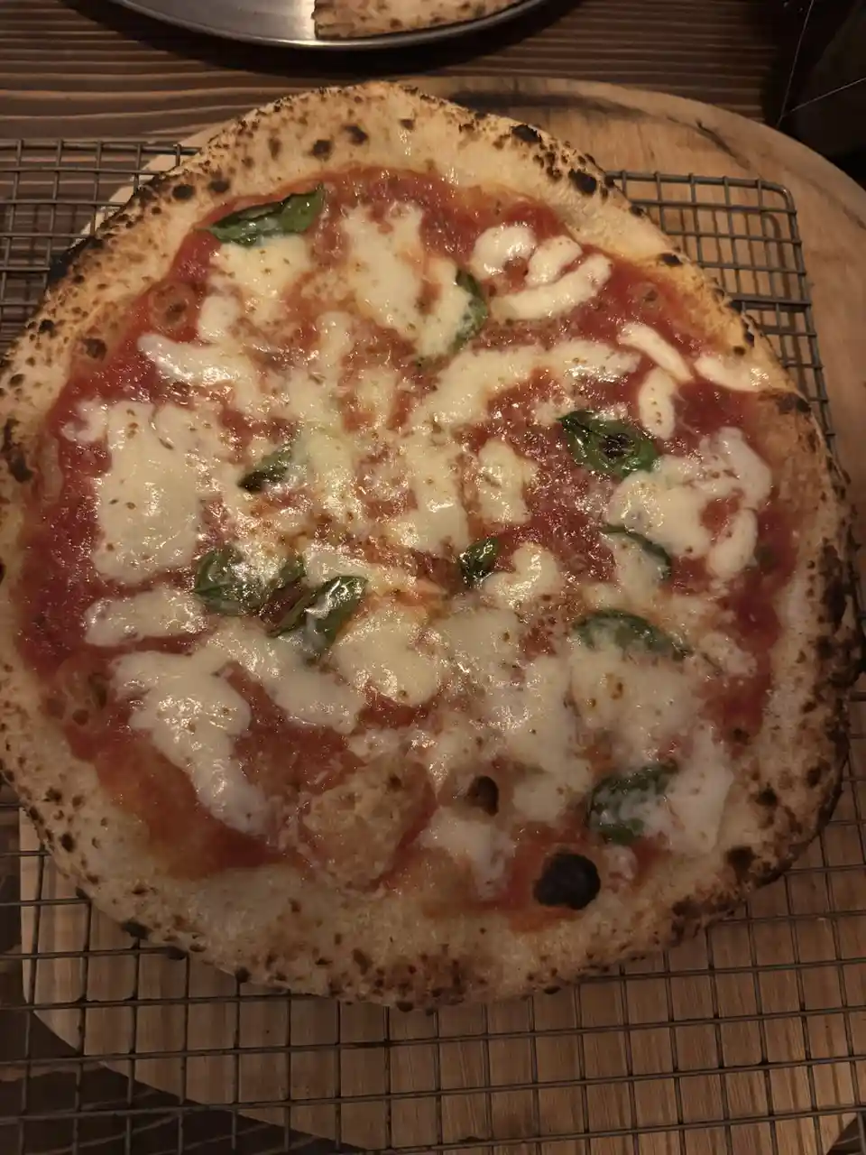 A close-up photo of a freshly baked Neapolitan-style pizza with charred crust, tomato sauce, melted mozzarella cheese, and…