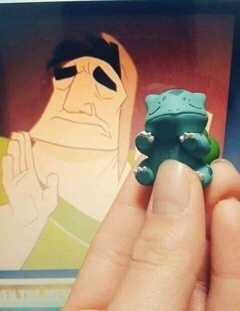 A hand holds a small green Pokémon figurine, resembling Bulbasaur, in front of a screen displaying an animated character…