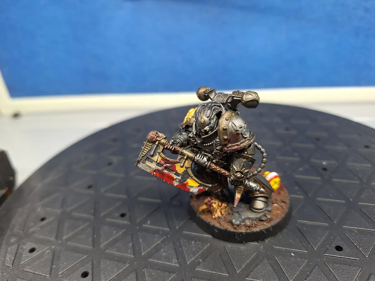 A heavily armored, grim-faced miniature warrior with a large, blood-stained axe stands on a circular, textured black base…