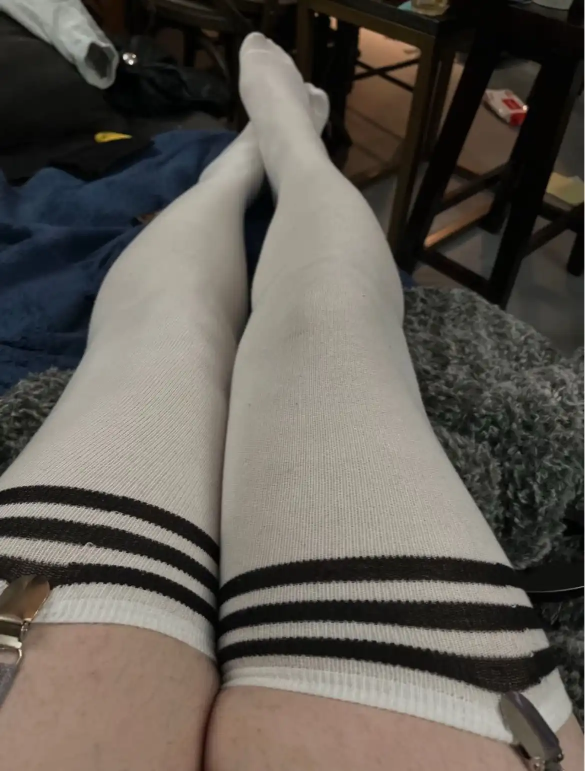 A close-up photo shows a person's legs clad in white thigh-high socks with three black stripes near the top, sitting on a…