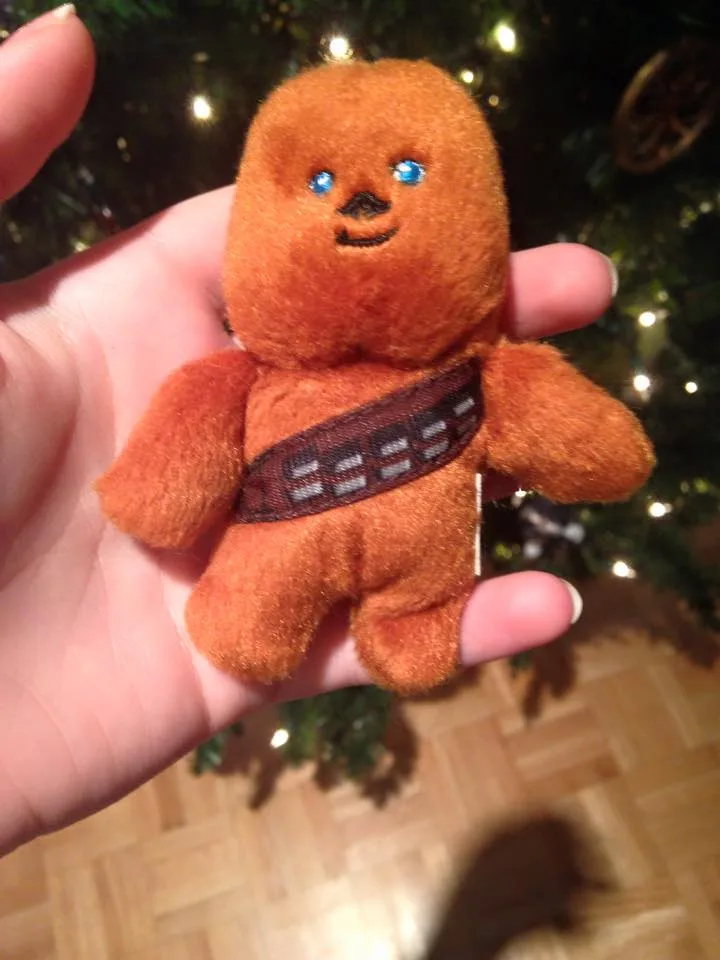 A small, orange, plush toy resembling the Star Wars character Chewbacca is held in a person's hand. The toy has blue eyes, a…