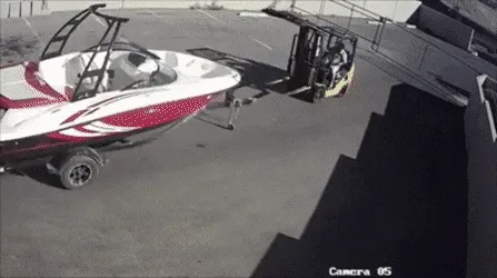 A security camera sequence shows a forklift attempting to lift a white and red speedboat on a trailer. The boat flips over…