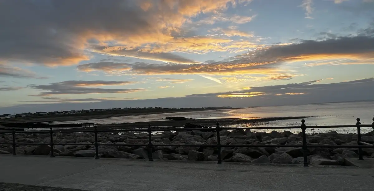 A scenic photo of a sunset over a coastal area with a railing and rocks in the foreground, overlaid with the text 'i'm not…