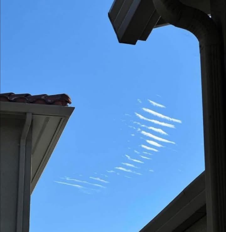 A low-angle shot shows a clear blue sky framed by the eaves and roofline of a house, with a distinct pattern of white, wispy…