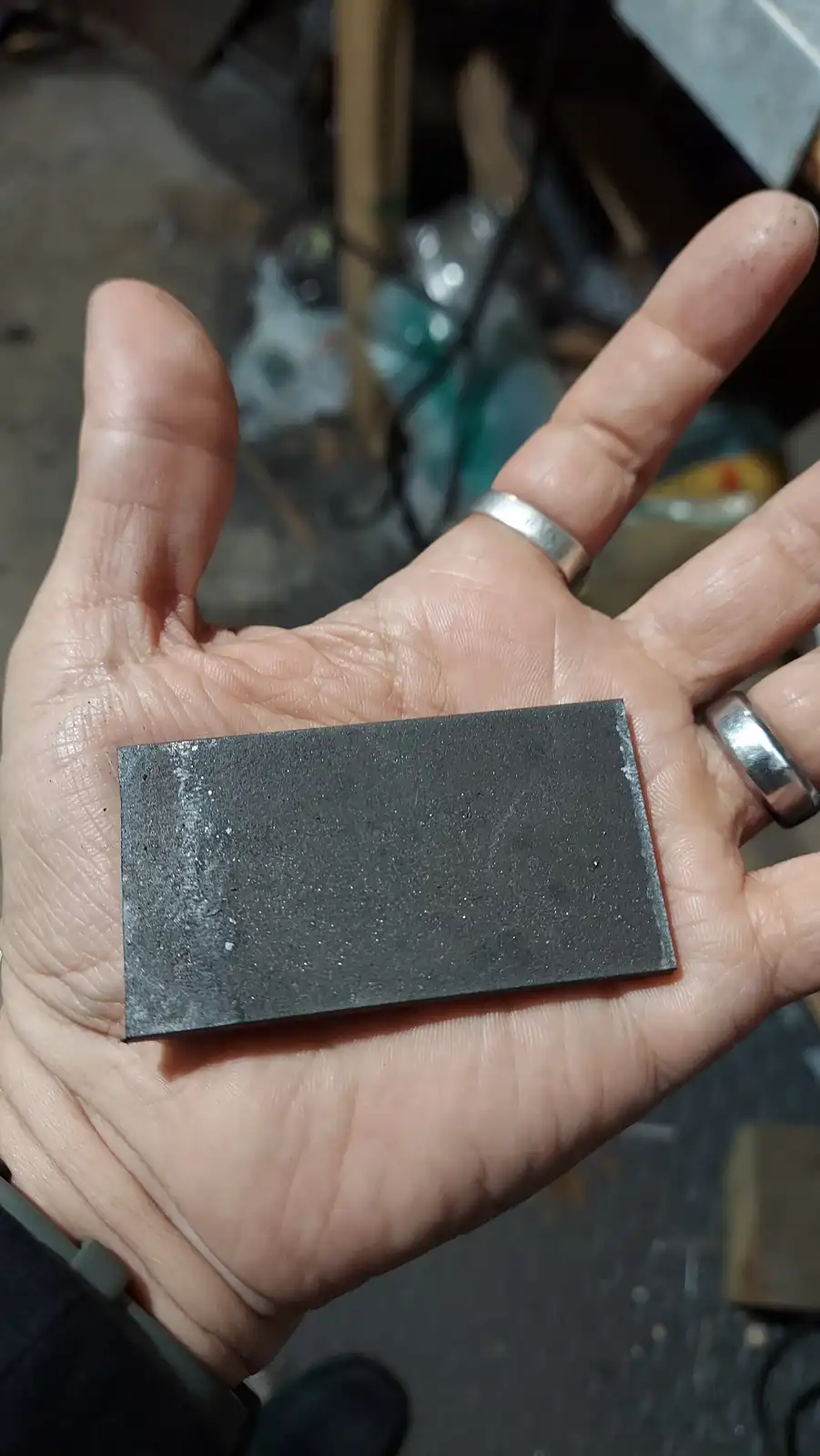 A person's open palm holds a small, dark gray rectangular object that resembles a business card but has a rough, speckled…