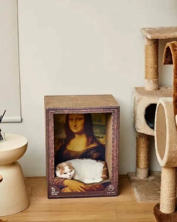 A white and ginger cat is curled up asleep in the lap of the Mona Lisa painting, which is displayed in a decorative frame on…
