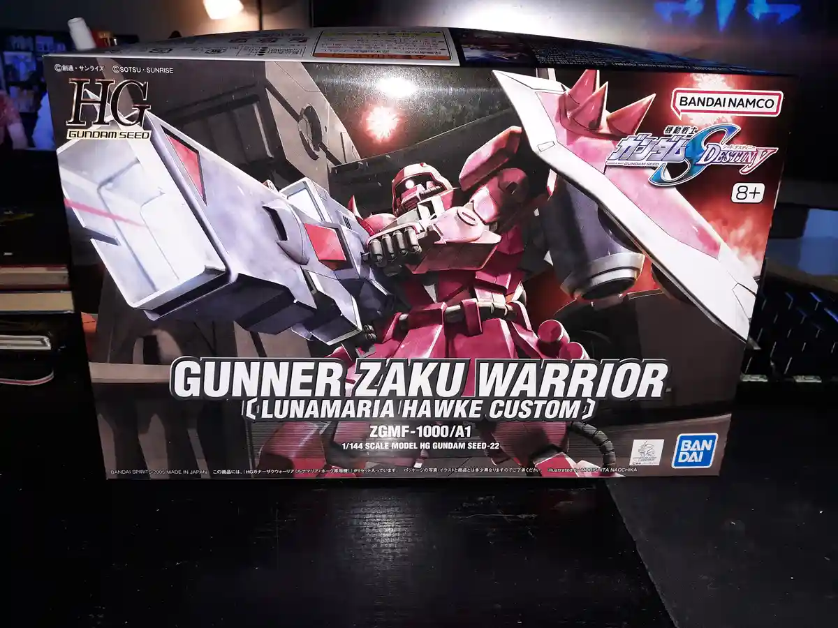 A photo of a Bandai HG Gundam Seed model box for the Gunner Zaku Warrior (Lunamaria Hawke Custom), featuring a red and white…