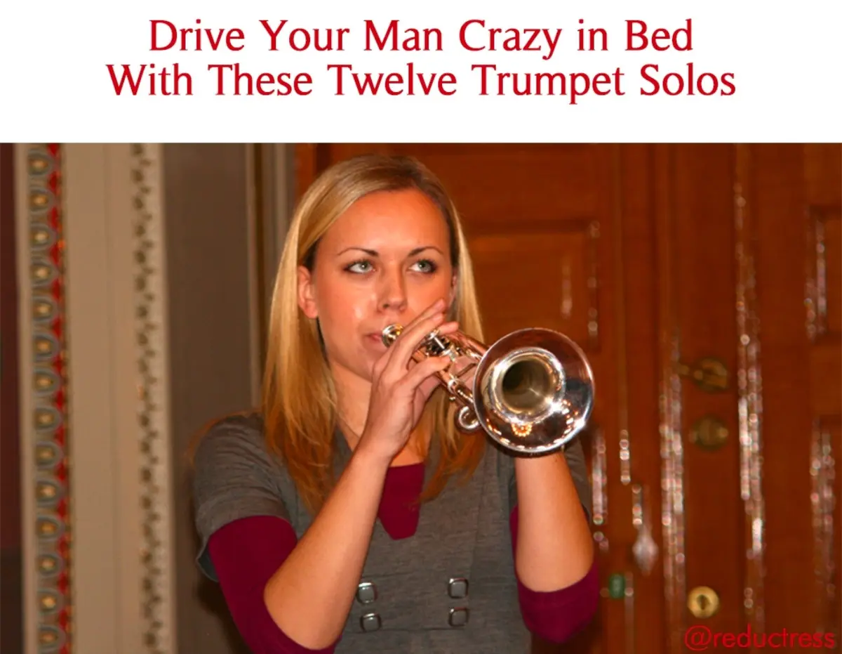 A woman with blonde hair is holding a shiny silver trumpet to her lips and appears to be playing it, wearing a grey vest…