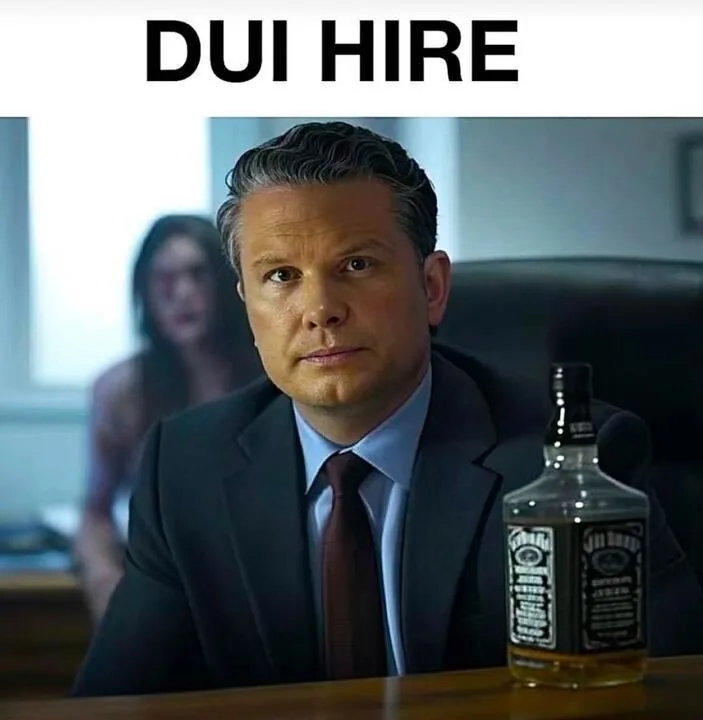 A man in a suit sits at a desk with a bottle of Jack Daniels whiskey beside him, looking serious. Behind him, a blurred…