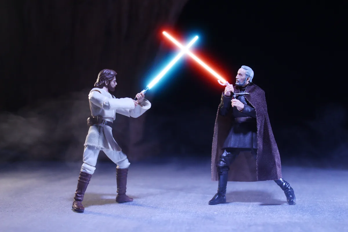 Two Star Wars action figures, one in white robes holding a blue lightsaber and one in dark robes holding a red lightsaber…