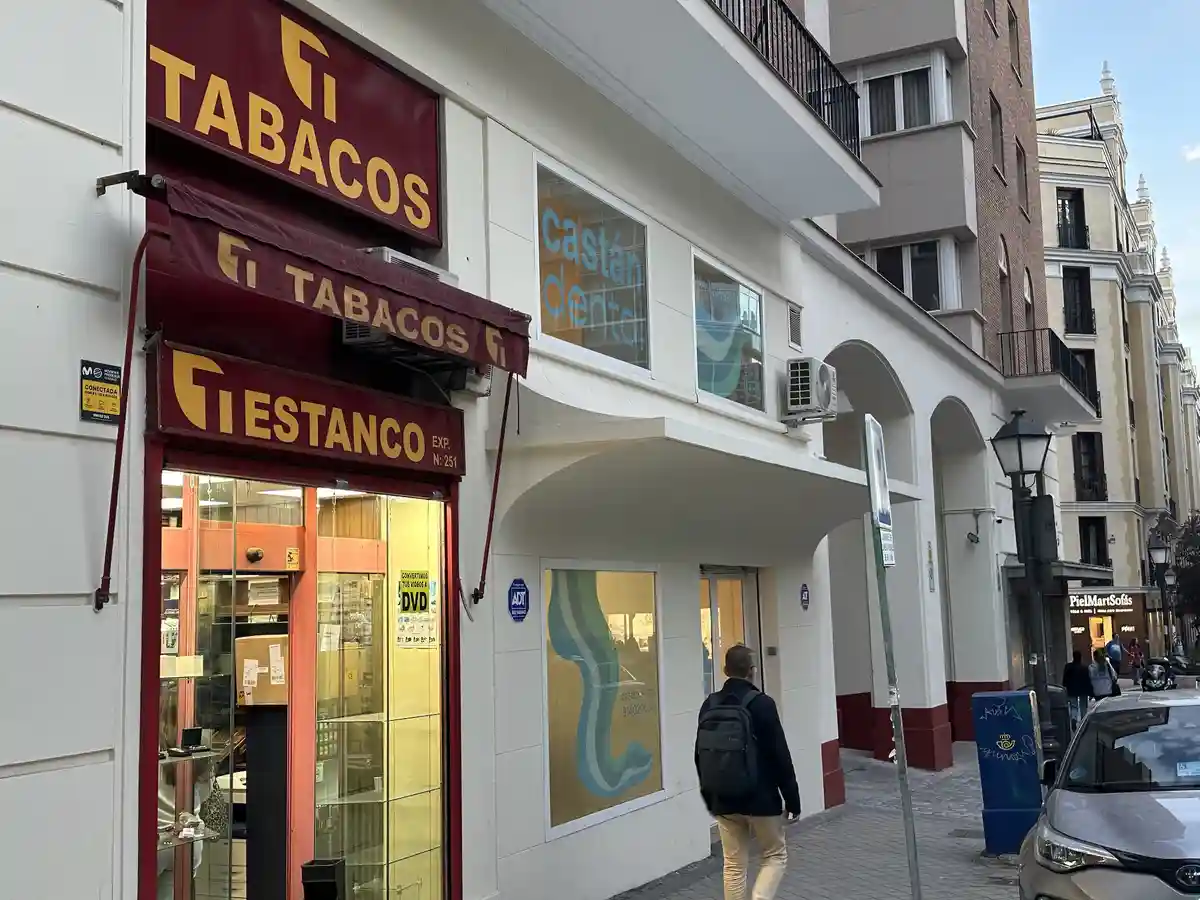 A street view shows a tobacco shop with a red awning and signage reading 'TABACOS' and 'ESTANCO'. A man walks past the shop…