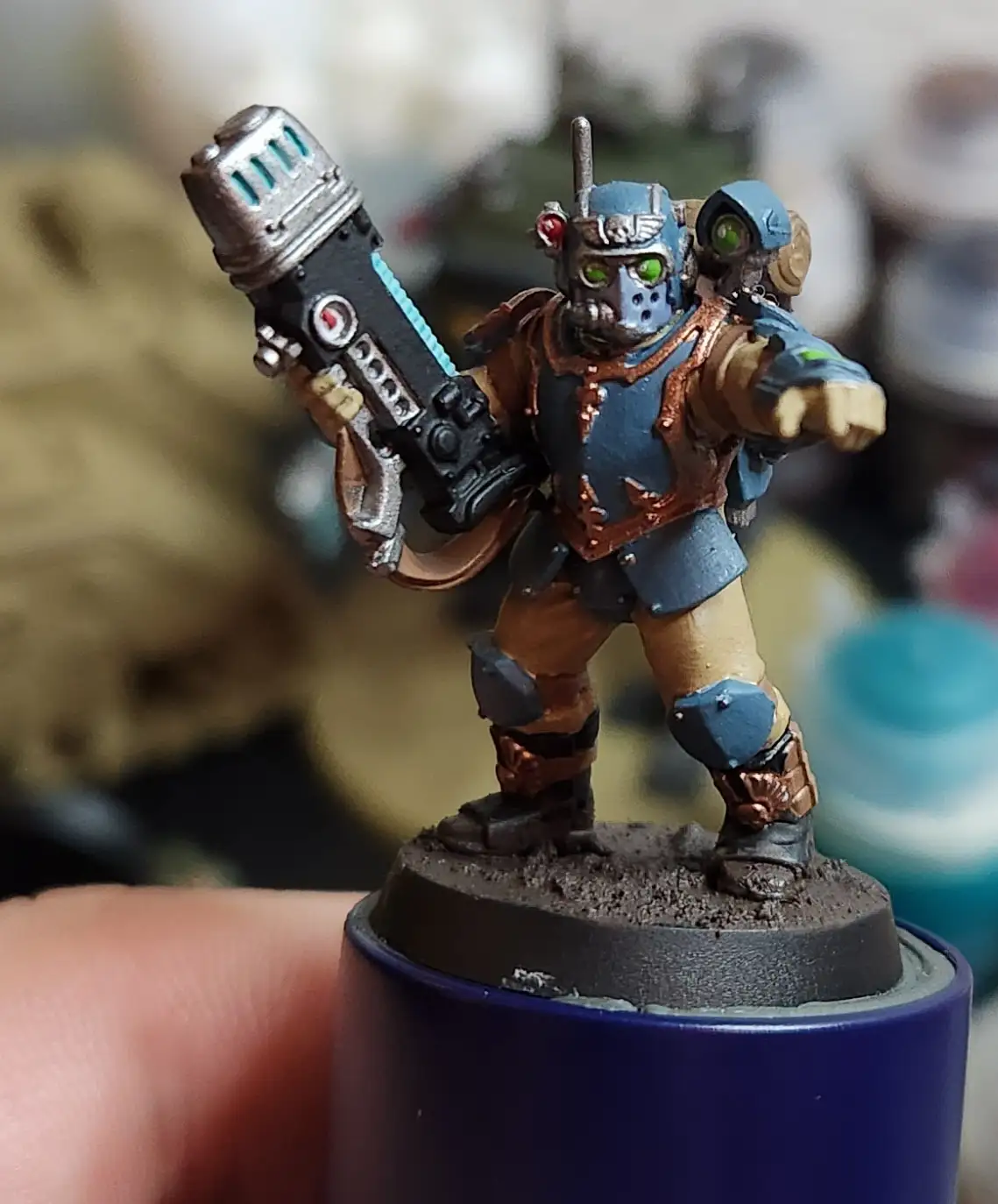 A close-up photo of a painted miniature figurine of a futuristic soldier with glowing green eyes, holding a large weapon…