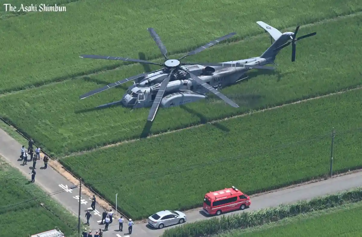 An aerial photo shows a large gray military helicopter, marked with 'NAVY' and the number '60', crashed in a green rice…