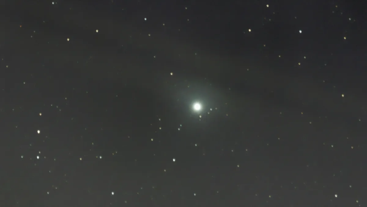 A dark night sky filled with numerous small, scattered stars, with one exceptionally bright, glowing celestial object…