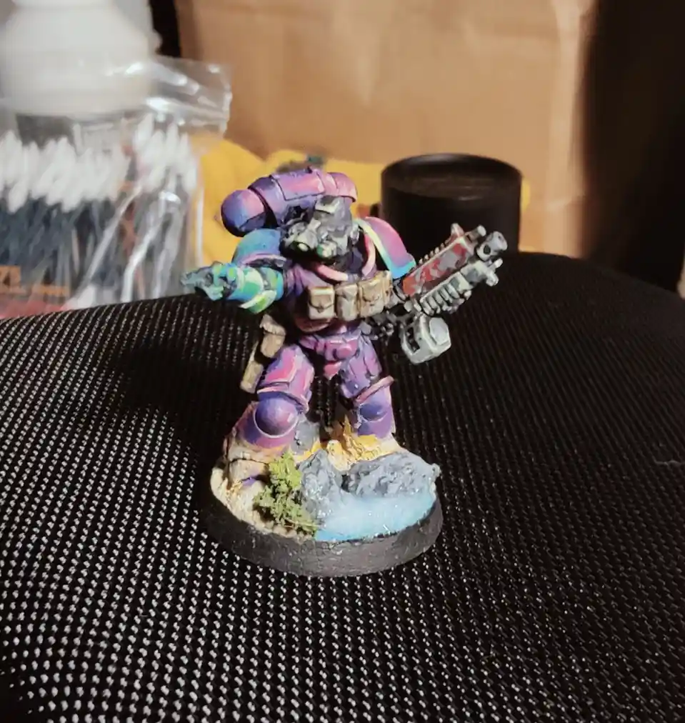A painted miniature figurine of a space marine, heavily customized with vibrant, mismatched rainbow colors across its armor…