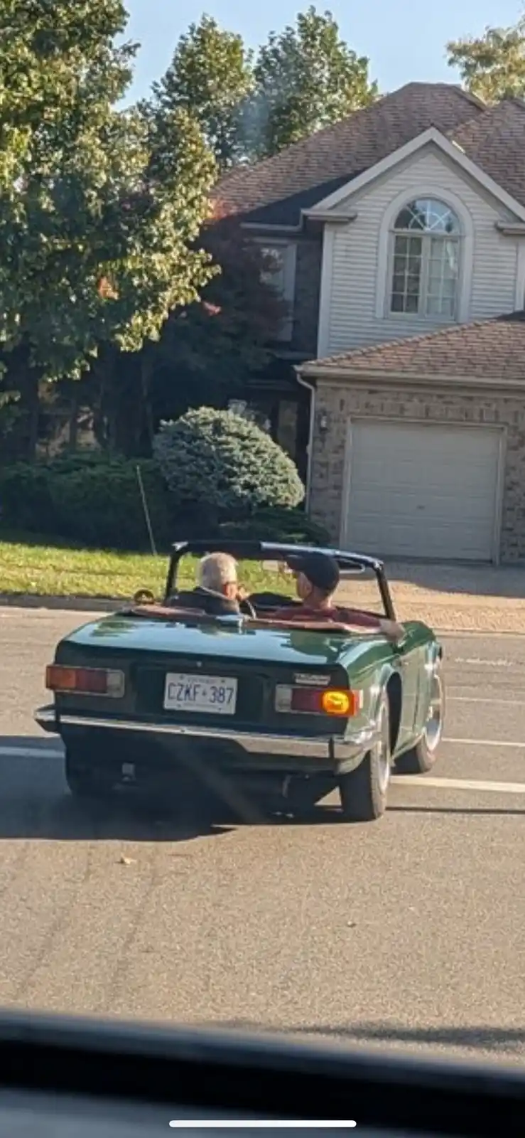 A green classic convertible with a visible Ohio license plate reading 'CZKF 387' is driving down a suburban street, with two…