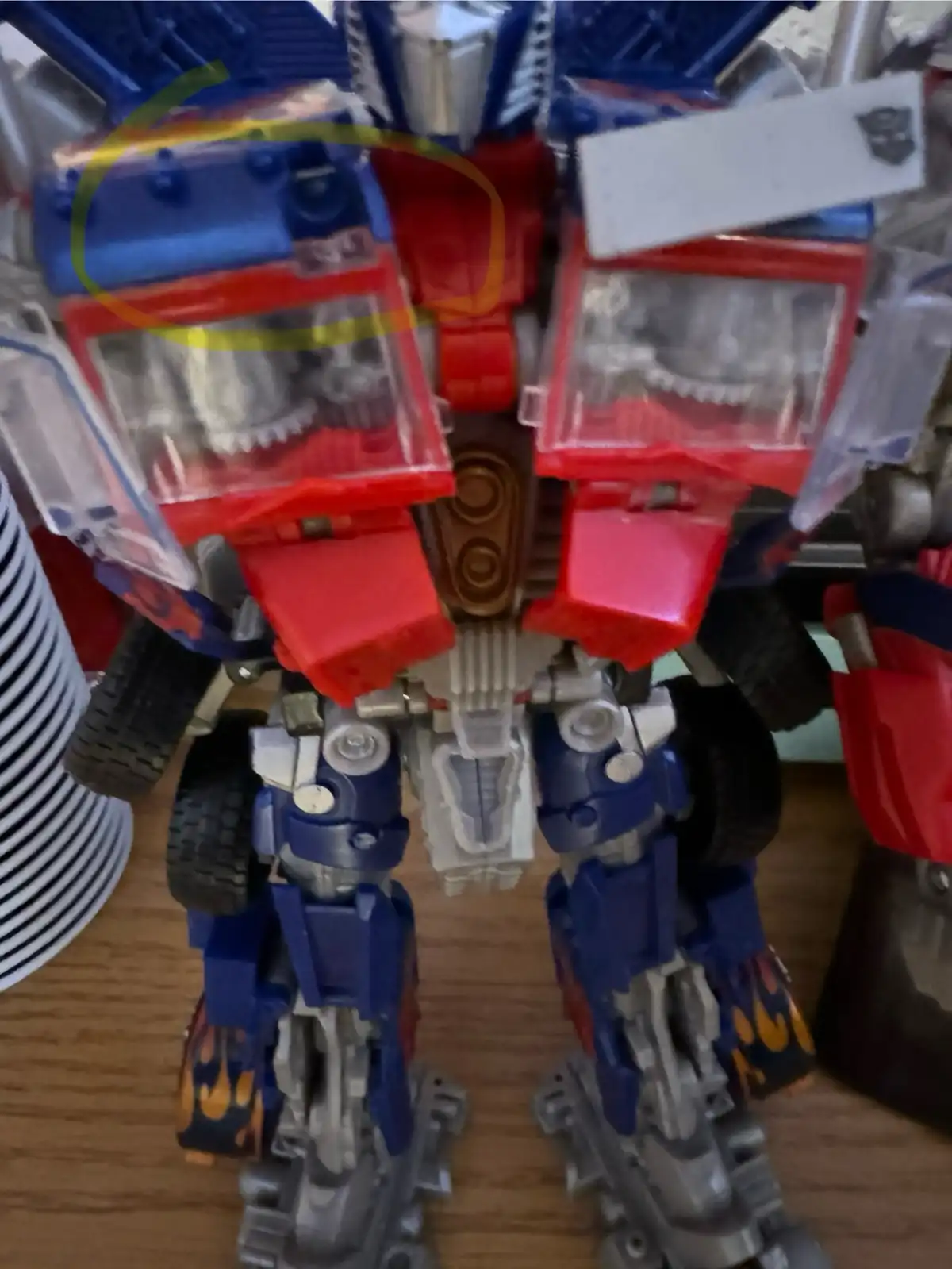 A close-up photo of a red, blue, and silver Optimus Prime toy, with a yellow circle drawn around a tiny, almost…