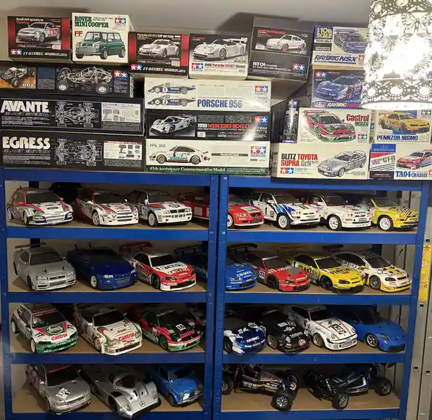 A blue metal shelving unit is filled with numerous radio-controlled (RC) car models, both in their original boxes on the top…
