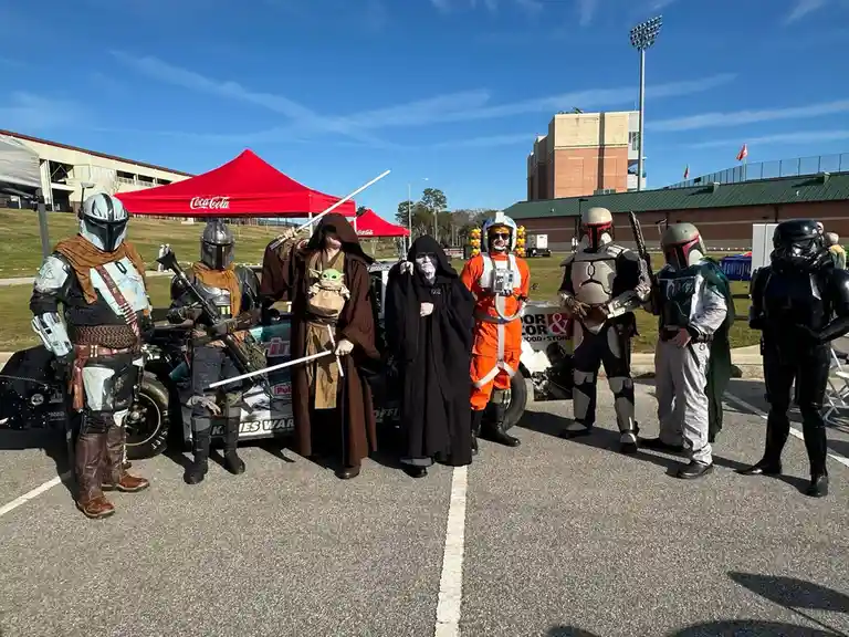 A group of people dressed as Star Wars characters, including The Mandalorian, Boba Fett, Darth Vader, and others, pose…