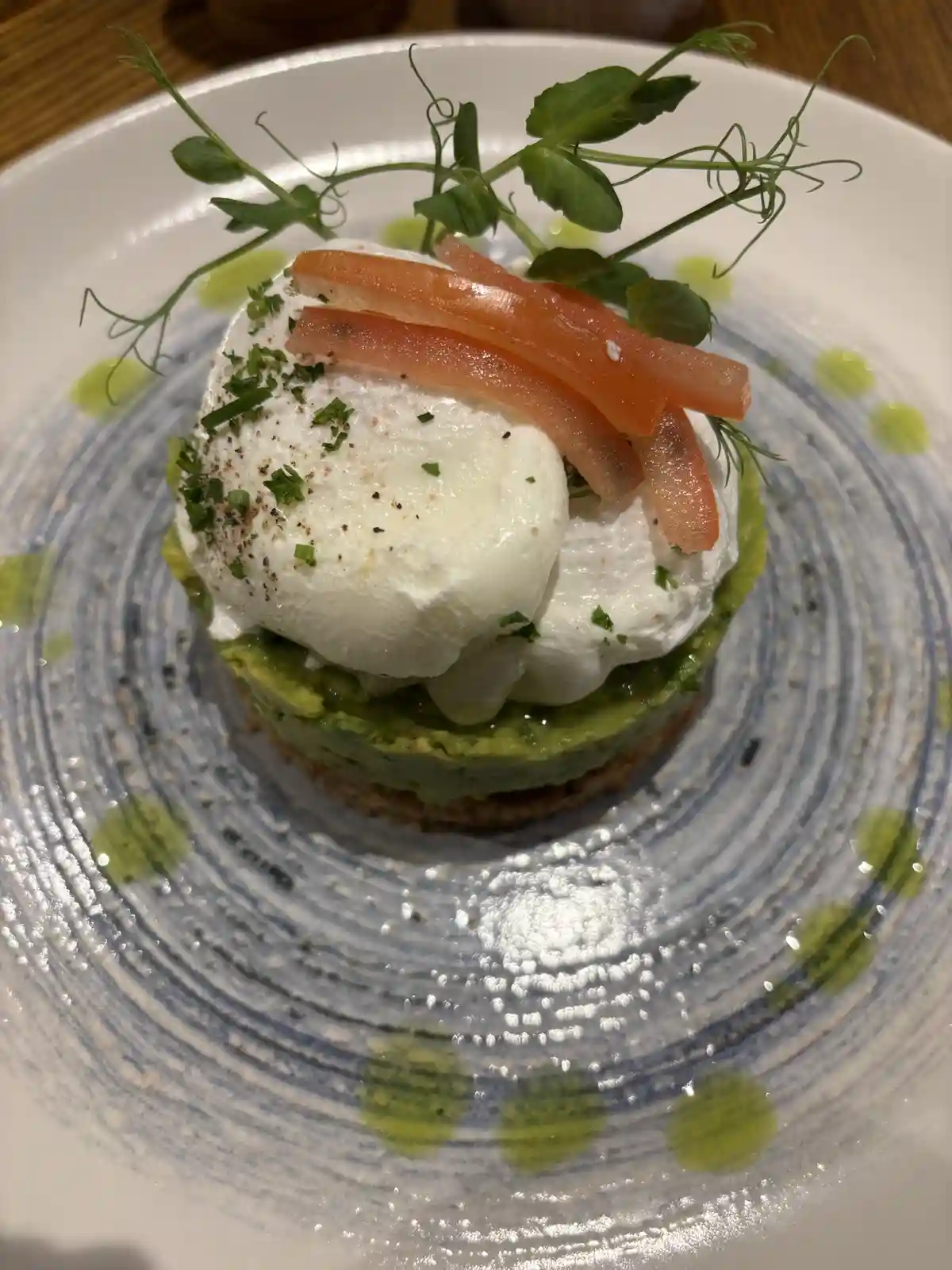 A close-up photo of a gourmet dish on a white plate with blue concentric swirls and green oil dots. The dish consists of a…