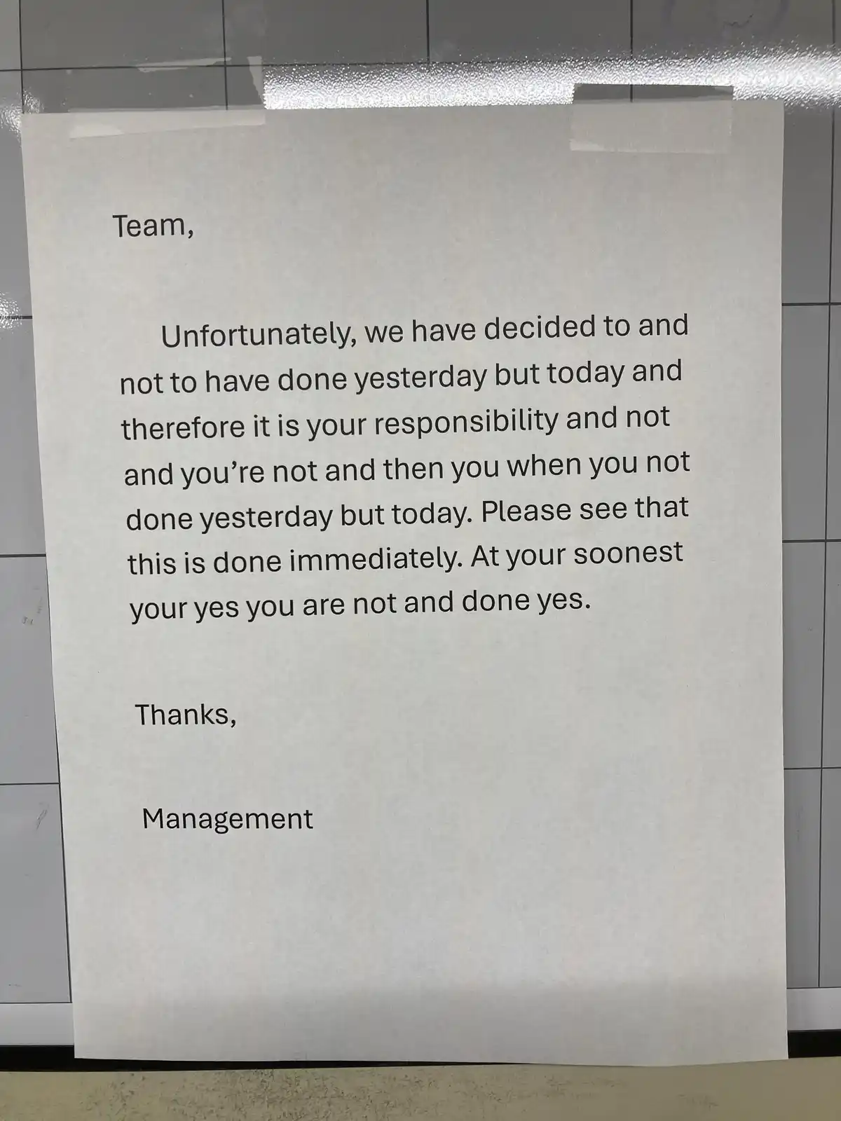 A piece of paper taped to a tiled wall contains a poorly written memo from 'Management' to 'Team' with nonsensical…
