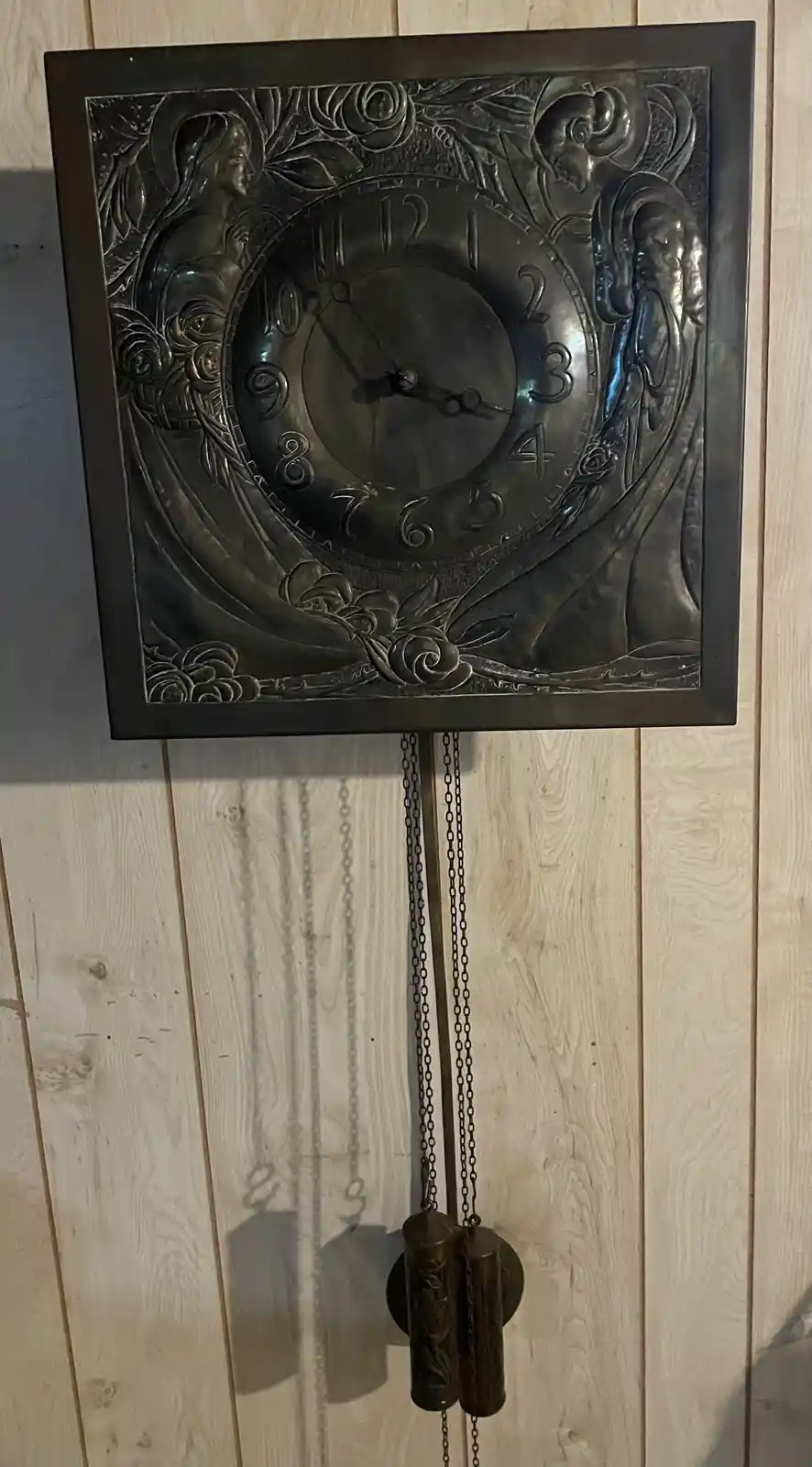 A vintage, ornate metal pendulum clock with Art Nouveau-style female figures and floral carvings around its face, mounted on…