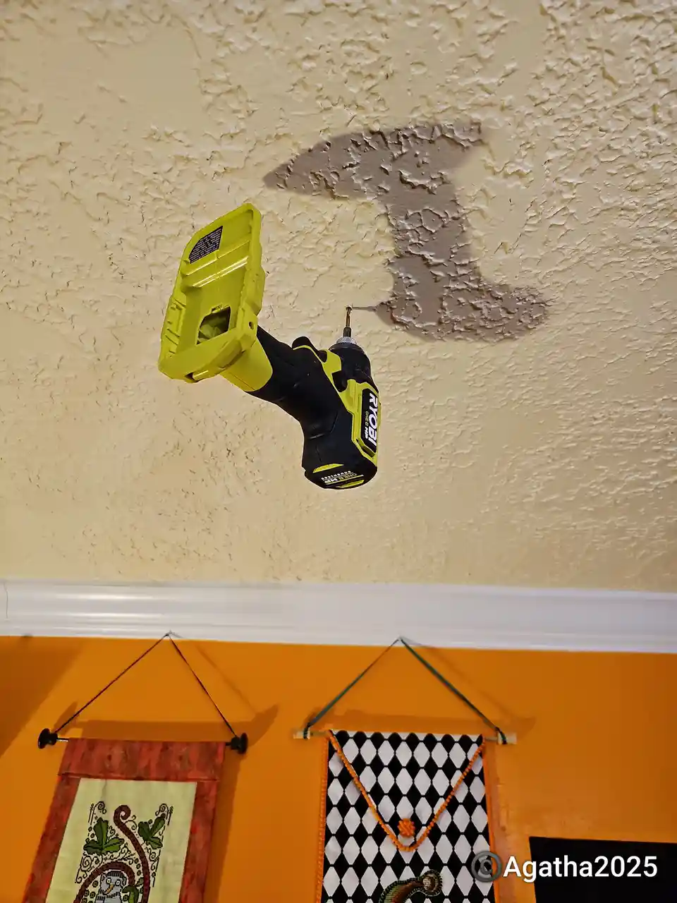 A yellow and black Ryobi power drill is suspended in mid-air, seemingly drilling into a patch of peeling paint on a textured…
