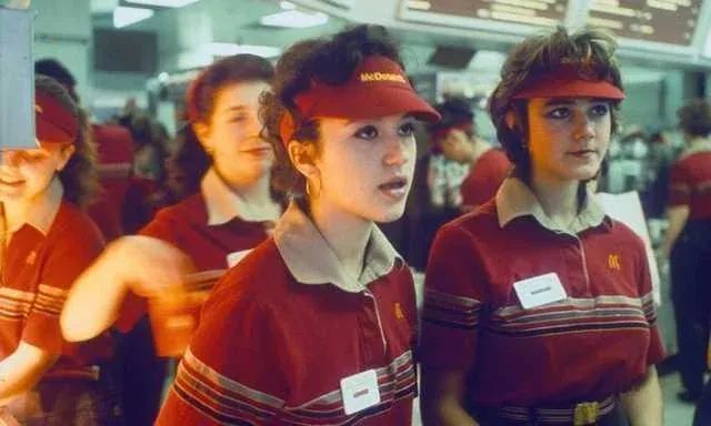 A vintage photo of several young women in 1980s McDonald's uniforms, including red polo shirts with striped collars and red…