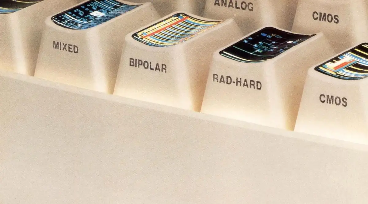 A close-up of a beige computer keyboard with keys labeled 'MIXED', 'BIPOLAR', 'RAD-HARD', and 'CMOS' (repeated). Each keycap…