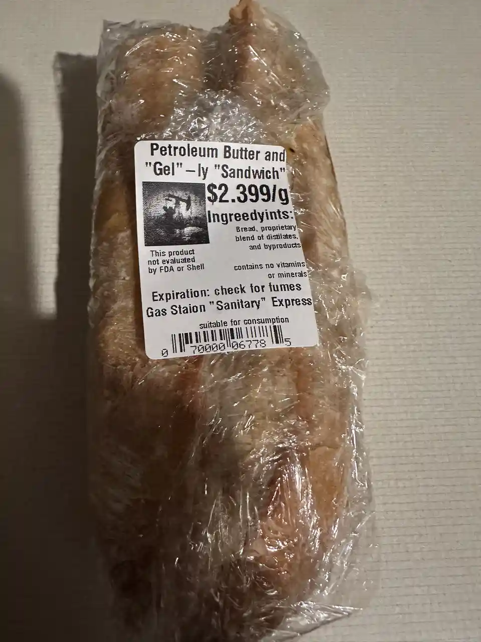 A close-up photo of a sandwich wrapped in clear plastic, featuring a mock product label that reads 'Petroleum Butter and…