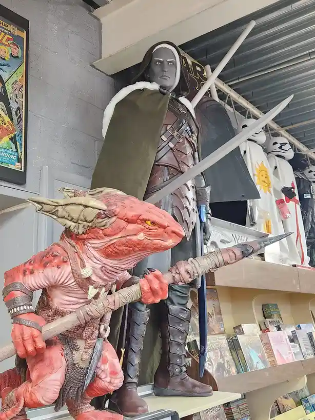 A large, realistic-looking statue of a human warrior in medieval armor and a green cloak stands behind a smaller…