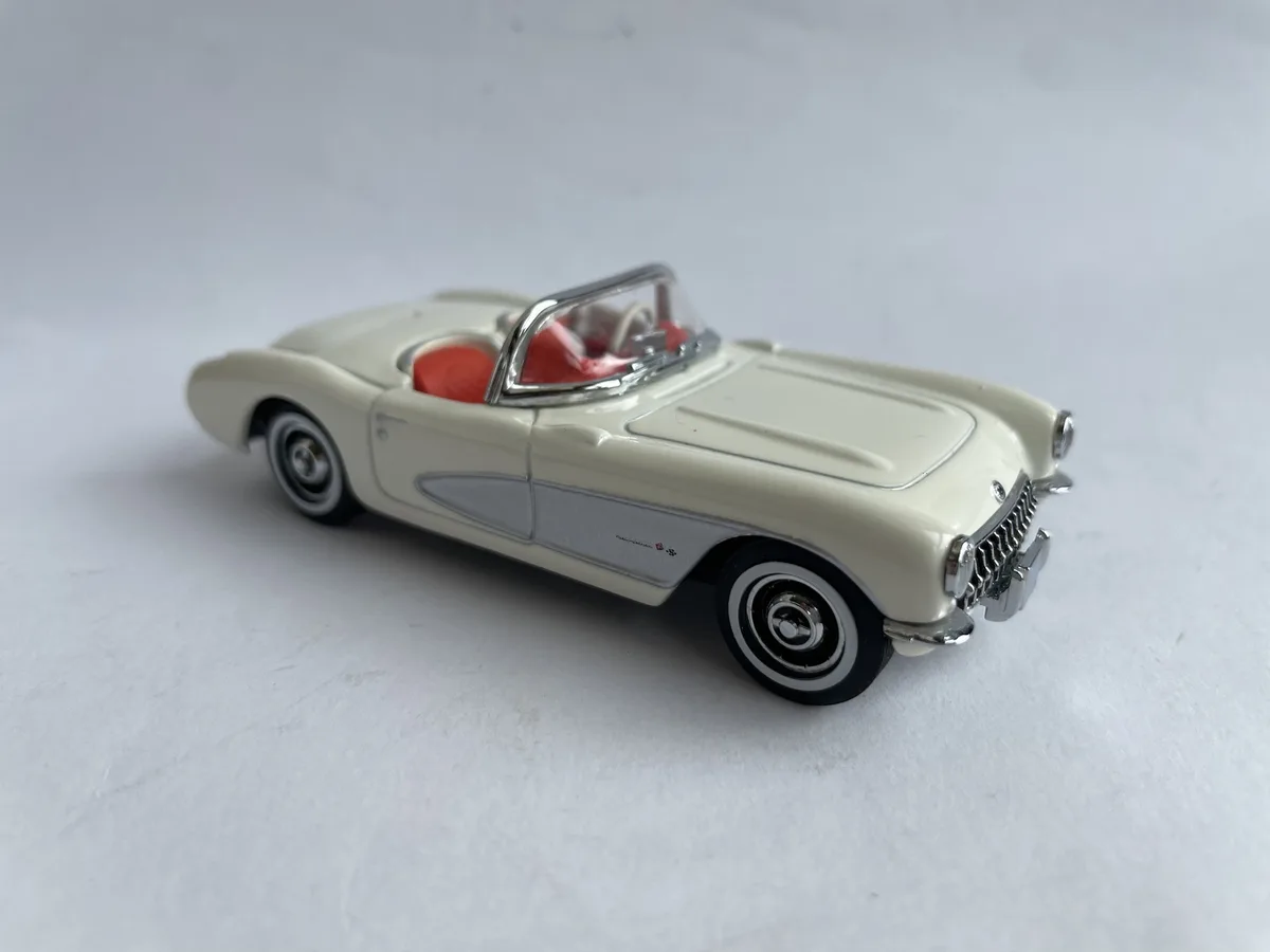 A cream-colored die-cast model of a classic 1950s Chevrolet Corvette convertible with red interior and chrome accents…