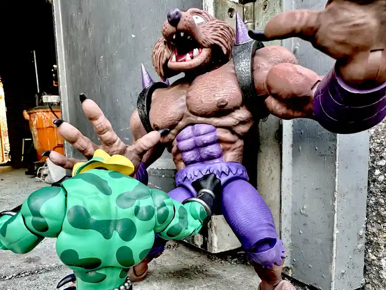 A muscular, brown, anthropomorphic badger action figure with purple armor and spiked shoulder pads is leaning against a…