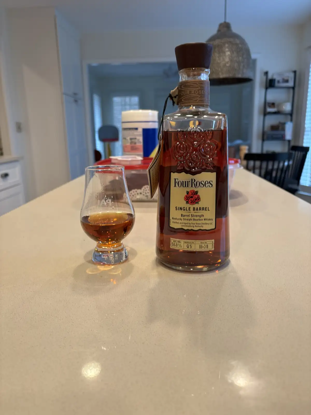 A bottle of Four Roses Single Barrel Bourbon Whiskey and a tasting glass filled with amber liquid sit on a light-colored…