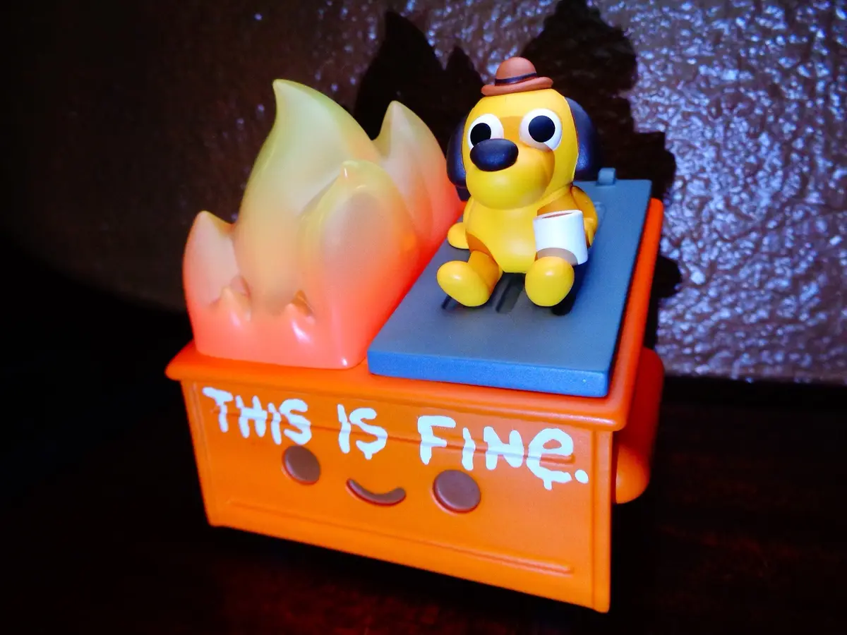 A small toy figure of a yellow dog wearing a brown hat and holding a white cup sits calmly on a blue platform atop an orange…