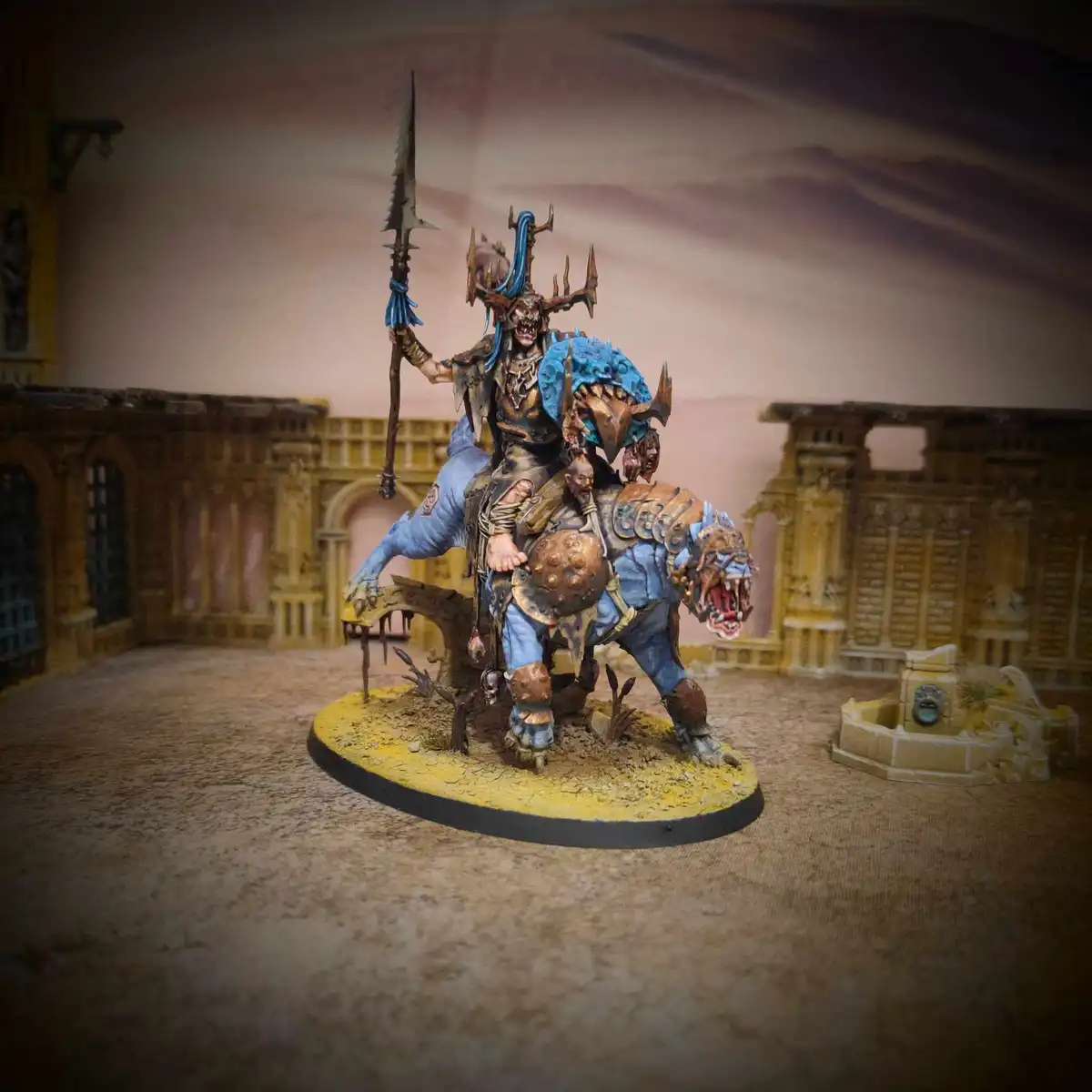 A highly detailed, painted miniature of a fantasy warrior riding a blue, armored, snarling beast, holding a spiked weapon…