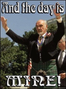 A man in a kilt and formal jacket stands outdoors with both arms raised in celebration, smiling broadly. The image has bold…