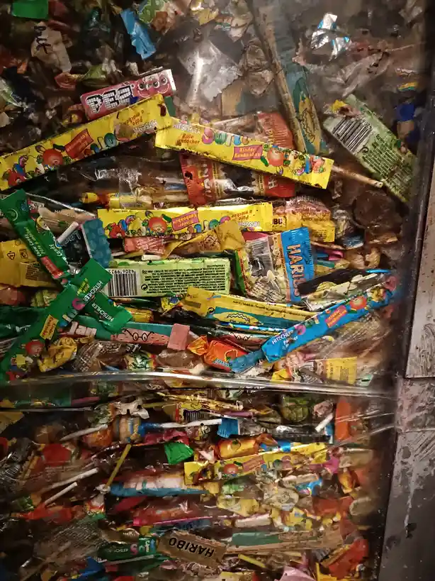 A close-up view of a vending machine's interior, completely filled with a chaotic pile of discarded, crushed, and stained…