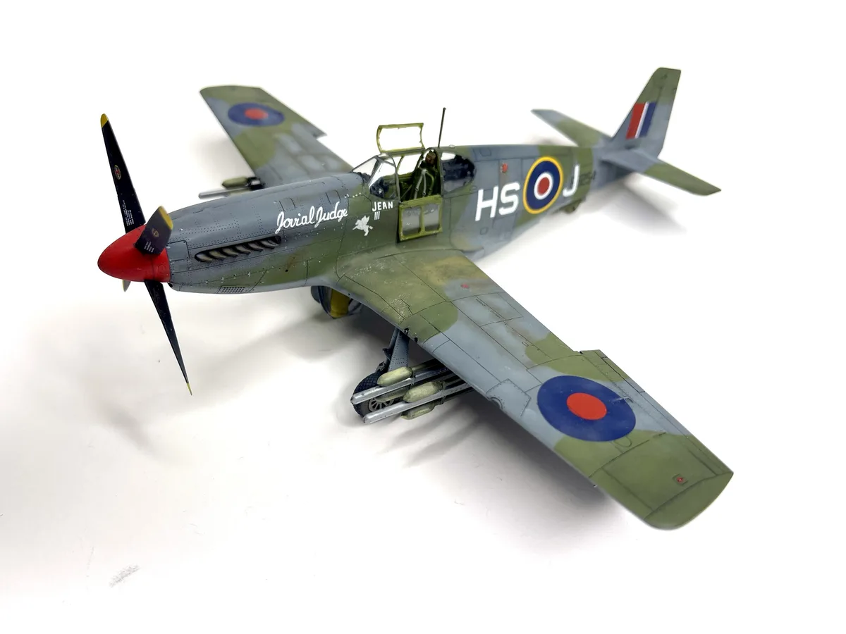 A detailed scale model of a British Supermarine Spitfire fighter plane, painted in olive drab and grey camouflage with Royal…