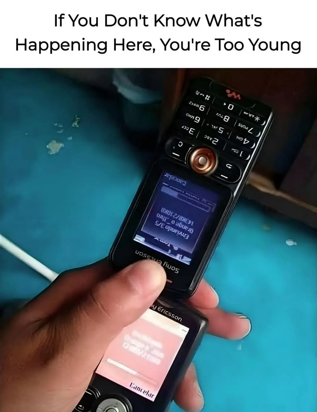 A hand holds an open Sony Ericsson flip phone, showing its screen with a file transfer progress bar and a 'Cancel' button on…