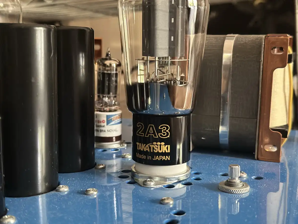 A close-up photo of a vintage vacuum tube labeled '2A3 TAKATSUKI Made in JAPAN' mounted on a blue chassis with other tubes…