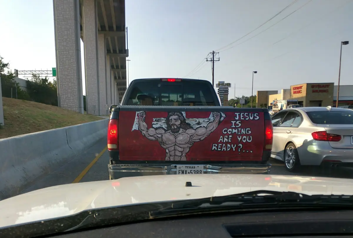 A photo taken from inside a car shows the rear of a black pickup truck with a red painted tailgate. The tailgate features a…