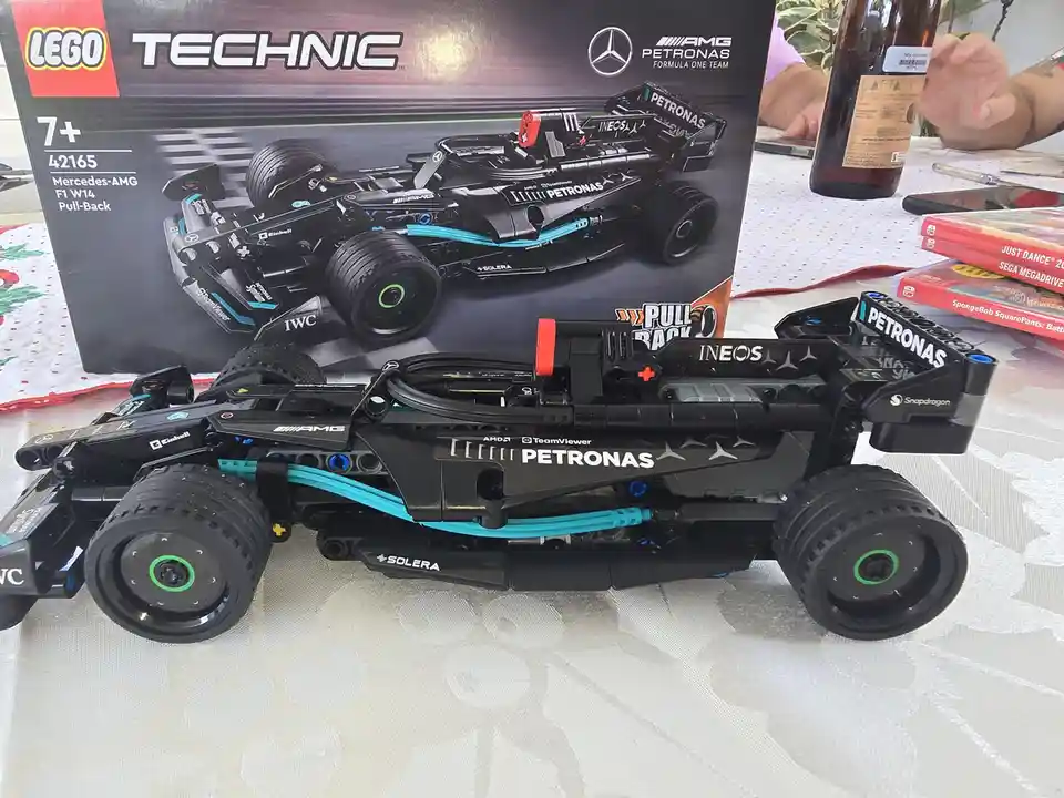 A completed LEGO Technic Mercedes-AMG F1 W14 Pull-Back race car sits on a table in front of its box, with visible sponsor…