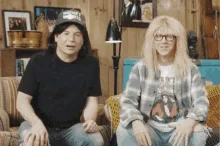 A six-panel sequence shows two men sitting on a couch. The man on the left wears a black t-shirt and cap, while the man on…