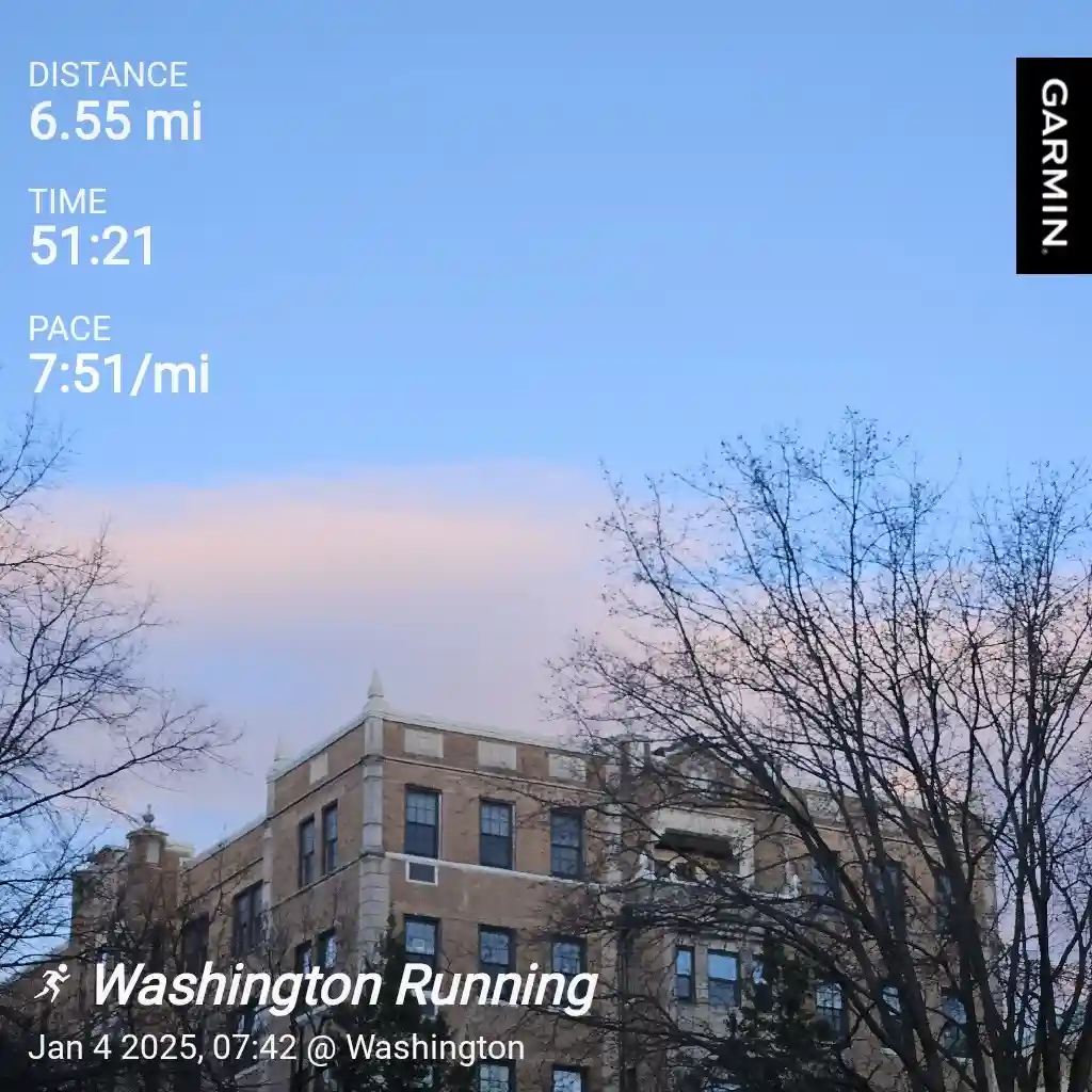 A screenshot of a Garmin running app overlay on a photo of a brick building with bare trees against a blue sky with pink…