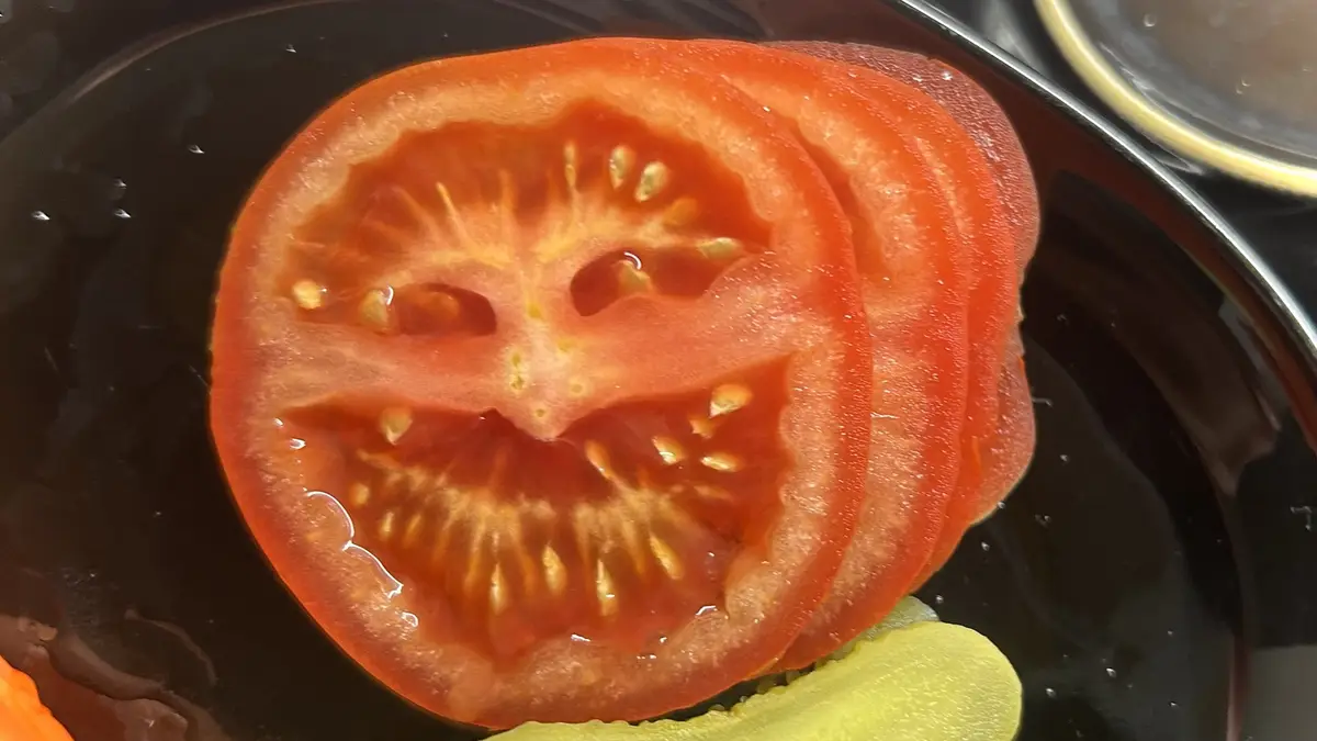 A close-up photo shows several slices of red tomato on a dark plate, with the top slice's internal structure forming a…