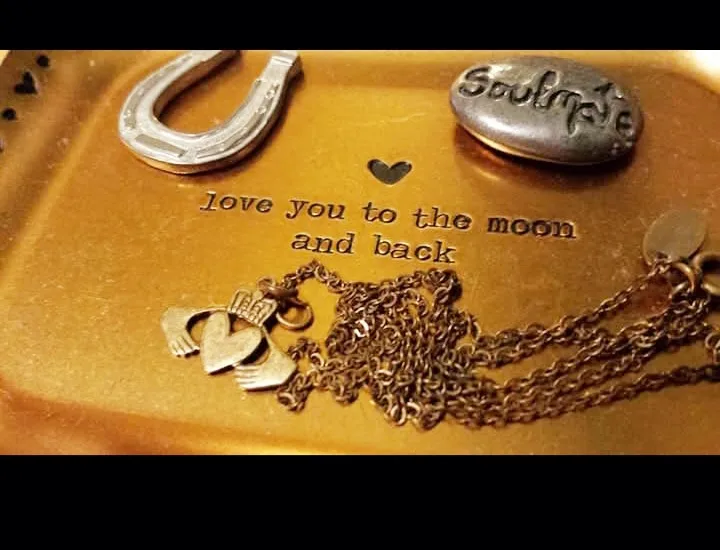 A close-up photo of a golden tray holding sentimental items including a horseshoe, a stone engraved with 'Soulmate', a…