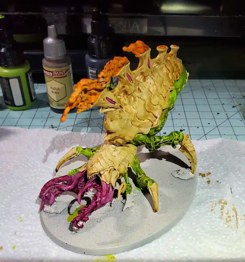 A painted miniature model of a grotesque, multi-limbed creature with a yellowish-brown, textured shell-like back, green…