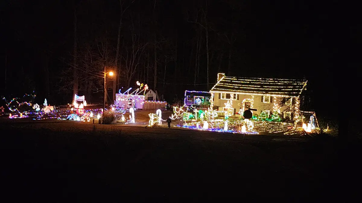A nighttime photo shows a house and yard extravagantly decorated with thousands of colorful Christmas lights and illuminated…