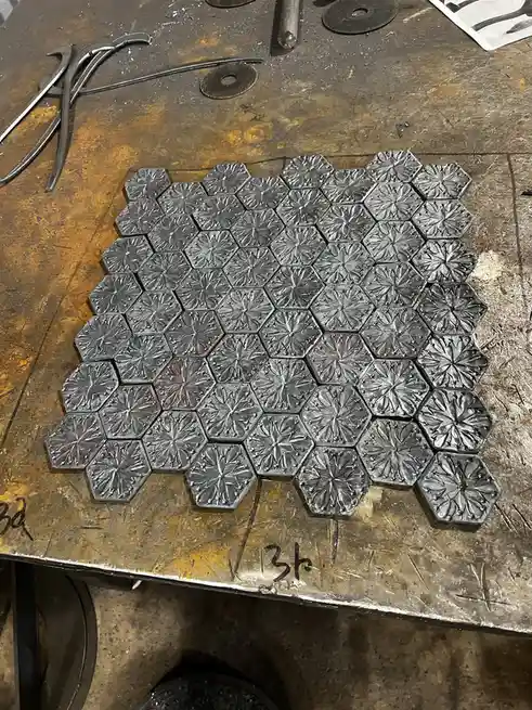 A collection of identical hexagonal metal pieces with embossed starburst patterns arranged on a worn workbench, with one…
